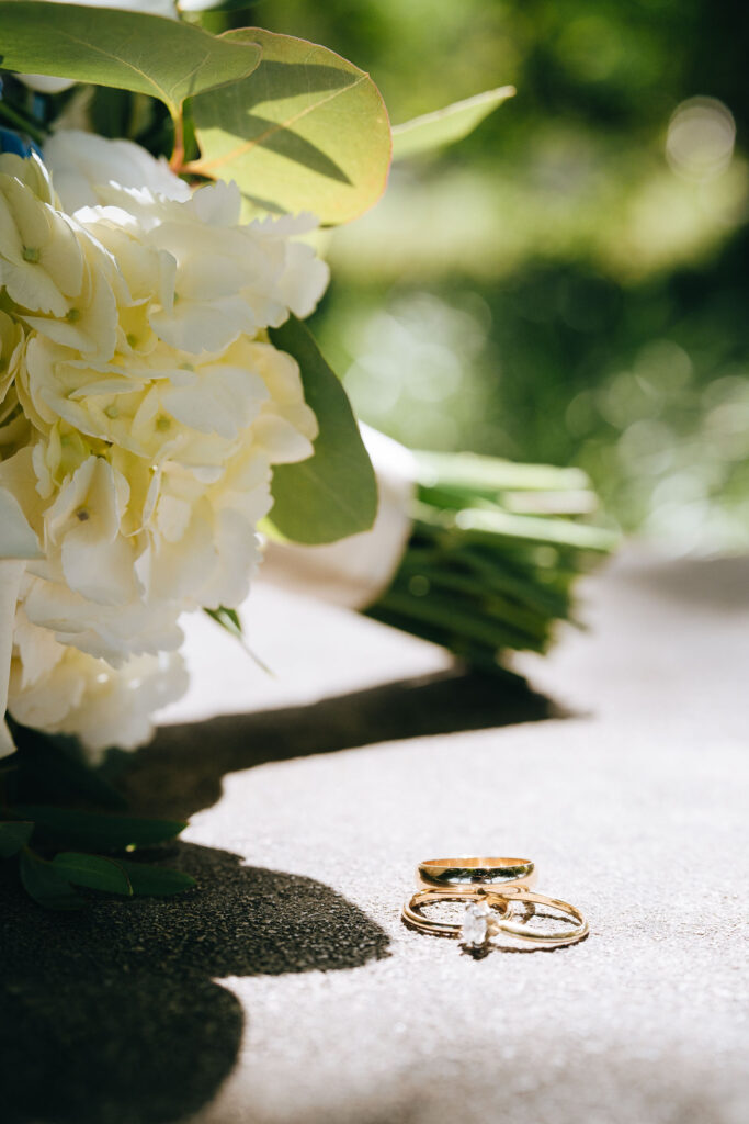 A pair of wedding rings with a wedding bouquet in the background