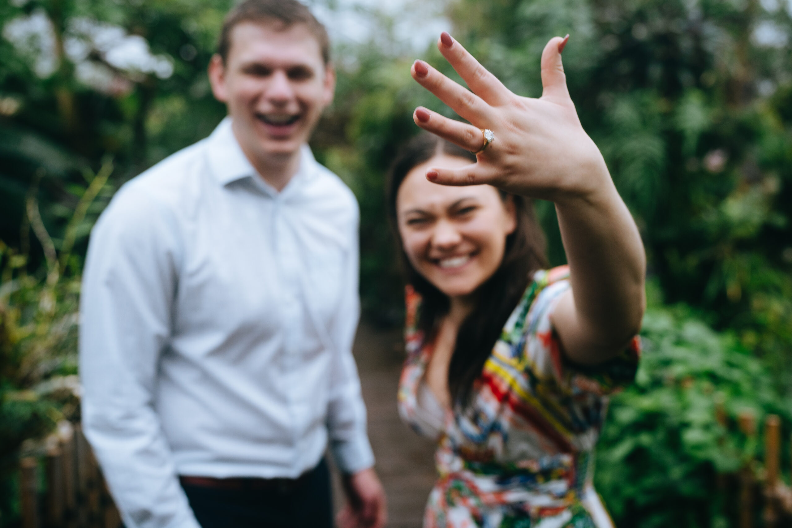 newly engaged woman standing next to her fiance while showing off her engagement ring