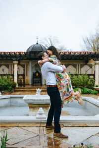 Man lifting fiancee in the air at the mobot garden while it's raining